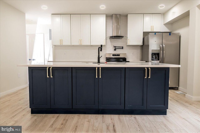 kitchen featuring wall chimney range hood, stainless steel appliances, white cabinetry, and a kitchen island with sink
