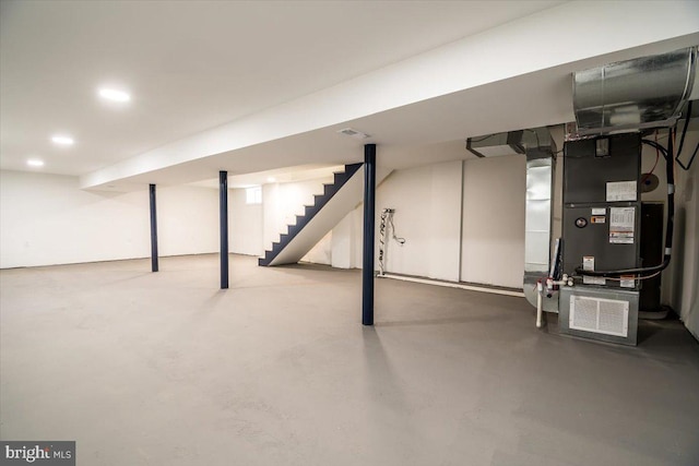 finished below grade area featuring heating unit, recessed lighting, stairs, and visible vents