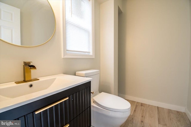 half bath with vanity, baseboards, toilet, and wood finished floors