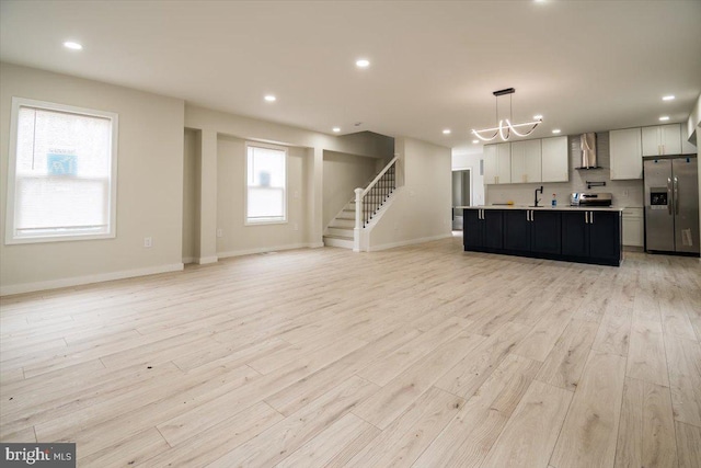 unfurnished living room with light wood-type flooring, stairs, baseboards, a notable chandelier, and recessed lighting