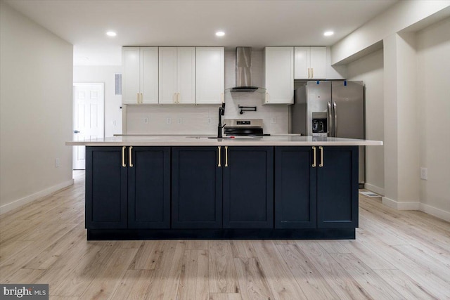 kitchen with an island with sink, light countertops, wall chimney exhaust hood, white cabinetry, and backsplash