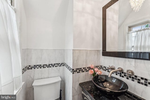 half bath featuring a notable chandelier, wainscoting, vanity, toilet, and tile walls