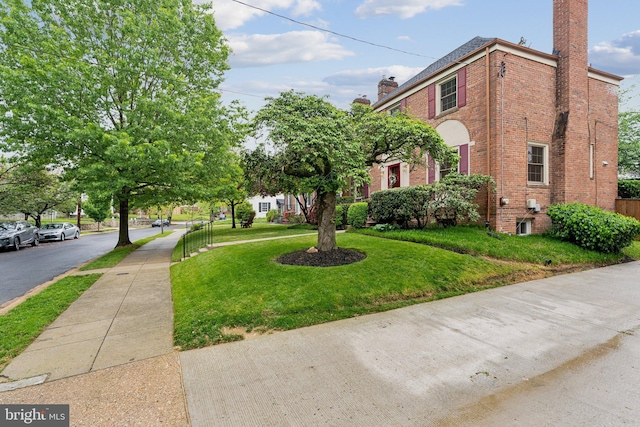 exterior space featuring brick siding, a chimney, and a front yard
