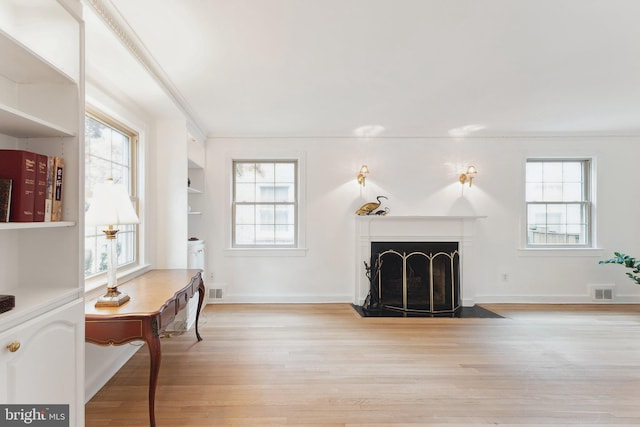 living area featuring plenty of natural light, ornamental molding, and light wood finished floors