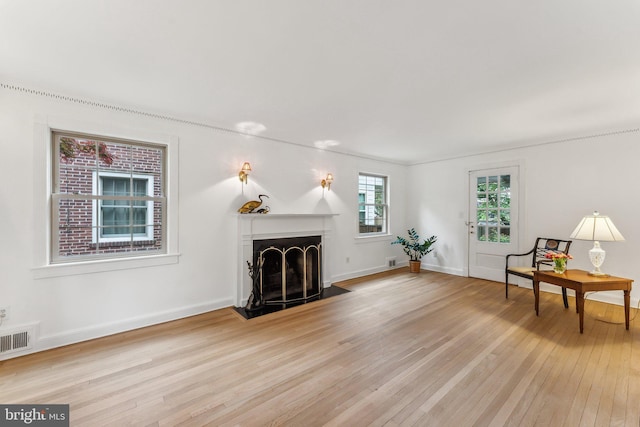 living room featuring visible vents, a fireplace with flush hearth, light wood-style floors, and baseboards