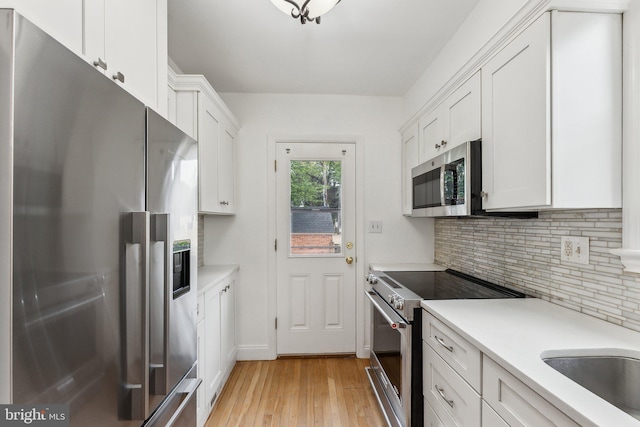 kitchen featuring appliances with stainless steel finishes, tasteful backsplash, light countertops, light wood finished floors, and white cabinetry