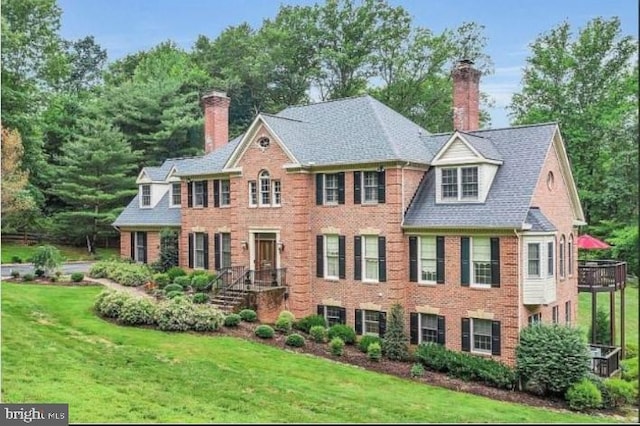 view of front of property featuring a chimney, a front yard, and brick siding