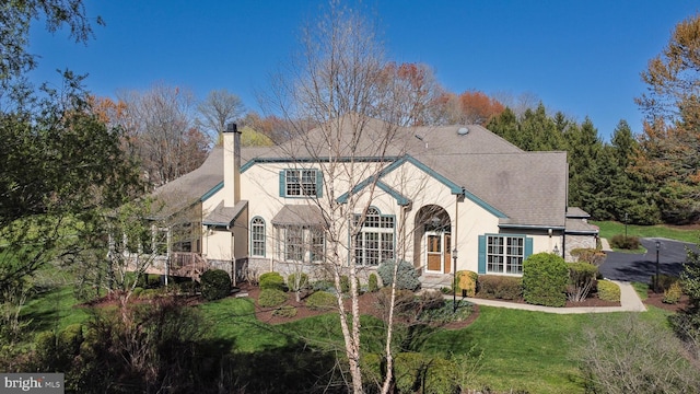 view of front of property with a shingled roof, stone siding, stucco siding, a front yard, and a chimney