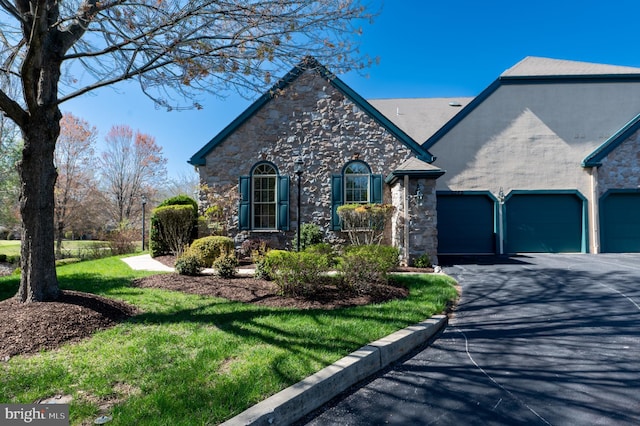 view of front of property with a front yard, a garage, stone siding, and aphalt driveway