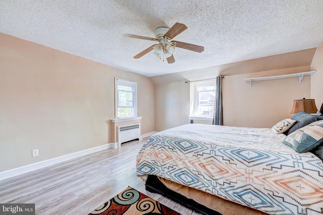 bedroom with radiator, wood finished floors, baseboards, a textured ceiling, and a ceiling fan