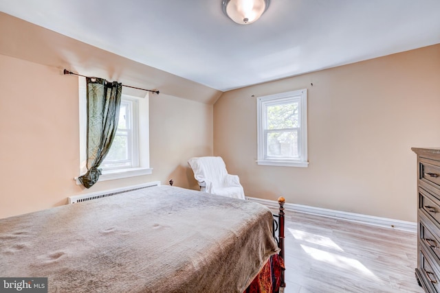bedroom with light wood-style floors, baseboards, a baseboard heating unit, and vaulted ceiling