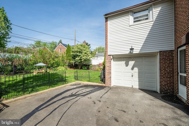view of side of home with a lawn, brick siding, fence, aphalt driveway, and an attached garage
