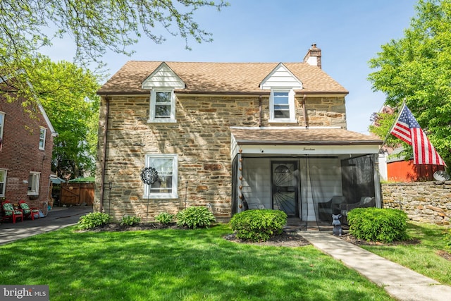 view of front of property with a chimney, roof with shingles, a front yard, fence, and stone siding