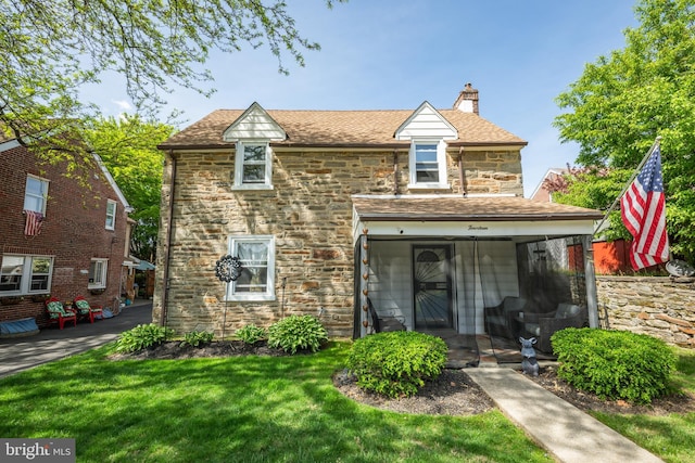 view of front facade with a chimney, a front yard, and stone siding