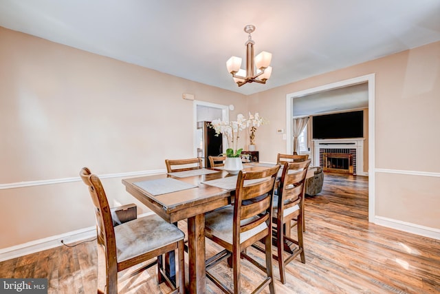 dining area with an inviting chandelier, baseboards, a brick fireplace, and light wood-style flooring