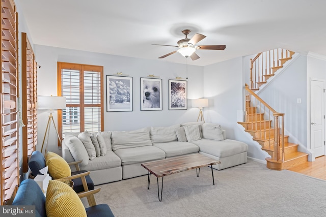 carpeted living room featuring stairs, baseboards, and a ceiling fan