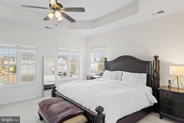 carpeted bedroom featuring a tray ceiling, baseboards, visible vents, and ceiling fan