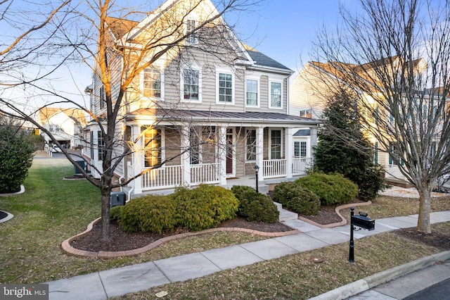 view of front of home featuring metal roof, covered porch, a front yard, and a standing seam roof