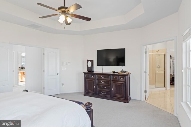 bedroom with ceiling fan, baseboards, a tray ceiling, light carpet, and ensuite bathroom