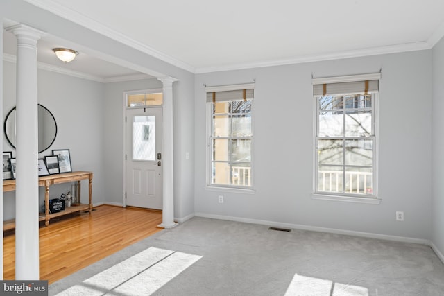 carpeted entryway with crown molding, decorative columns, visible vents, and baseboards