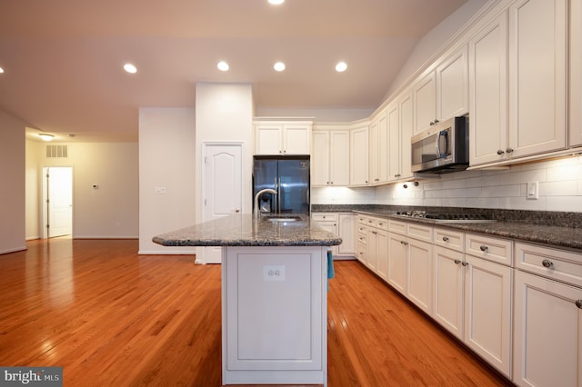 kitchen with visible vents, fridge with ice dispenser, black stovetop, stainless steel microwave, and backsplash