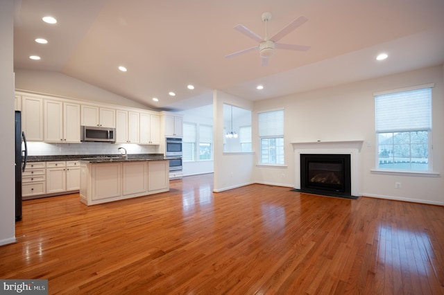kitchen featuring vaulted ceiling, open floor plan, dark countertops, a healthy amount of sunlight, and stainless steel appliances