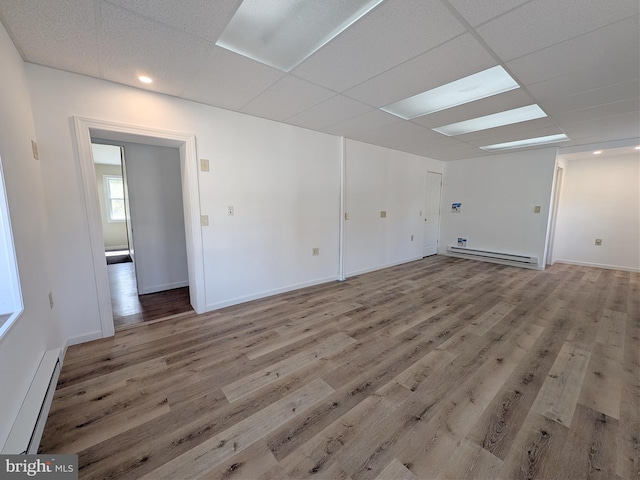 unfurnished room featuring a baseboard heating unit, baseboards, baseboard heating, a drop ceiling, and wood finished floors