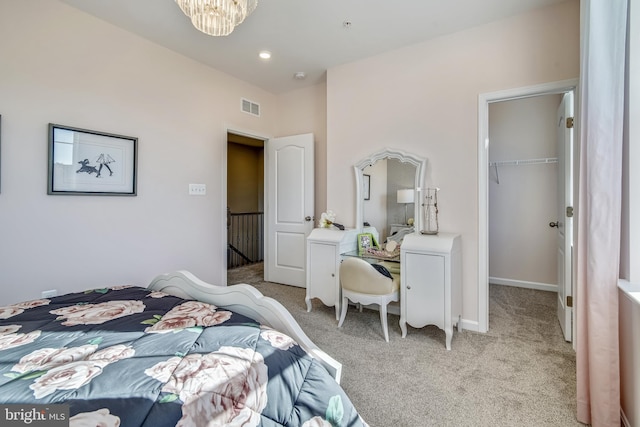 bedroom featuring visible vents, light colored carpet, a walk in closet, and a chandelier