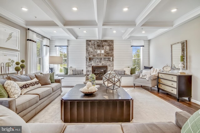 living room featuring beam ceiling, coffered ceiling, wood finished floors, a stone fireplace, and crown molding