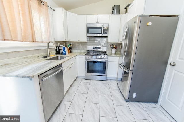 kitchen with light stone countertops, a sink, vaulted ceiling, and stainless steel appliances