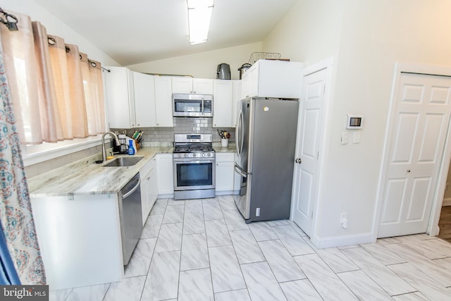 kitchen featuring vaulted ceiling, light stone counters, decorative backsplash, stainless steel appliances, and a sink