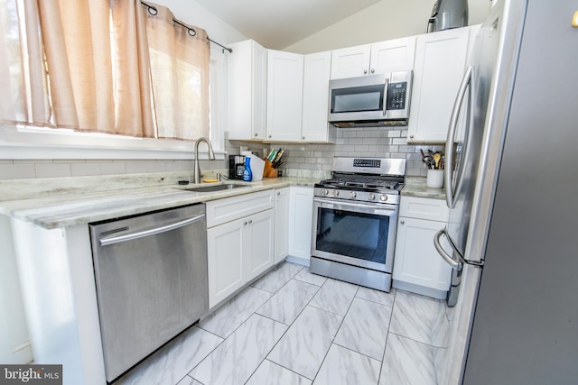 kitchen with tasteful backsplash, white cabinetry, lofted ceiling, stainless steel appliances, and a sink