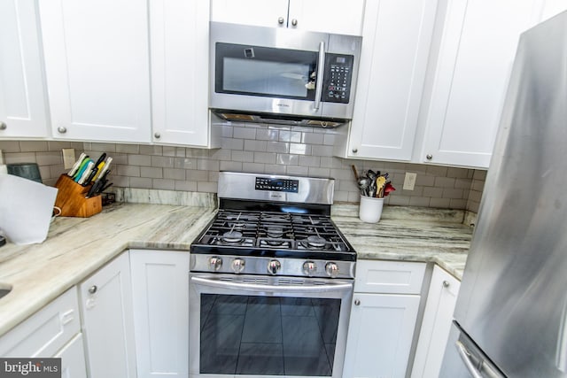 kitchen with stainless steel appliances, white cabinetry, backsplash, and light stone counters