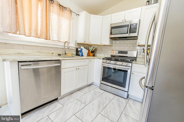 kitchen with white cabinetry, appliances with stainless steel finishes, a sink, lofted ceiling, and decorative backsplash