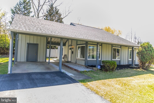single story home featuring a shingled roof, board and batten siding, driveway, and a front lawn