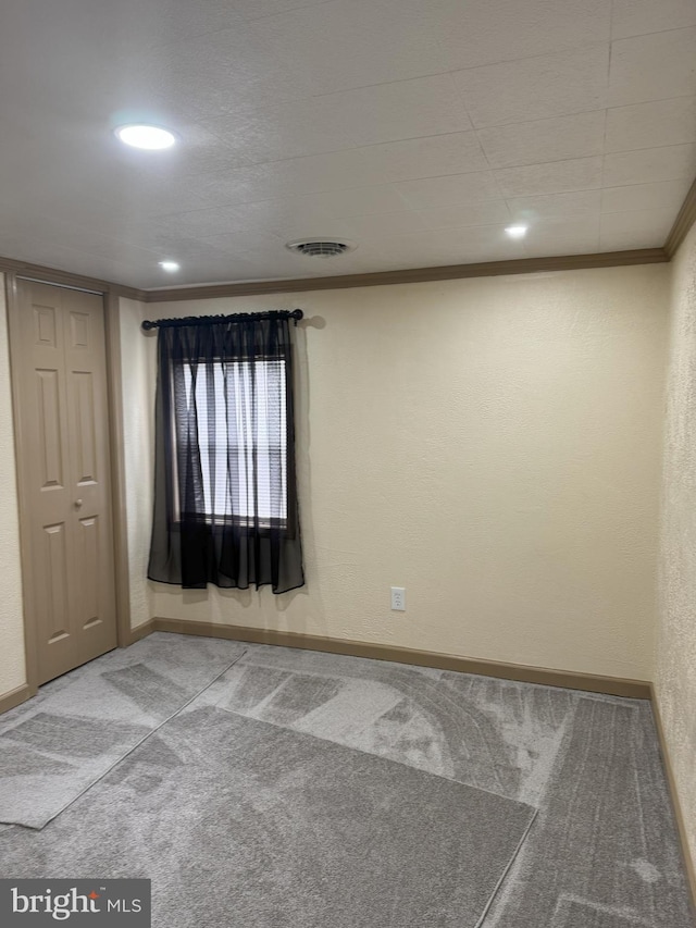 carpeted spare room with visible vents, baseboards, ornamental molding, and a textured wall