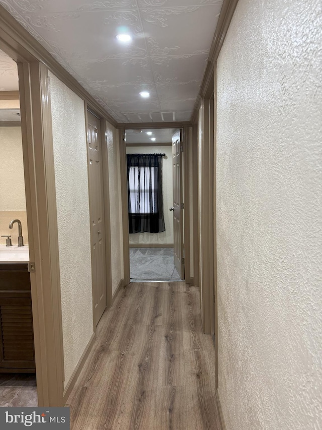 hallway featuring a sink, baseboards, wood finished floors, and a textured wall
