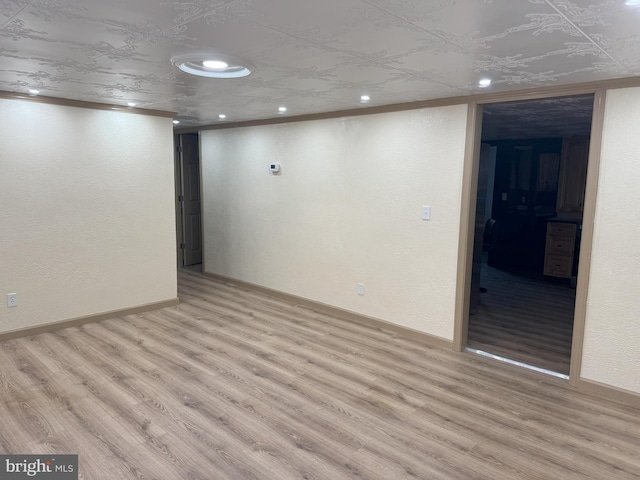 finished below grade area featuring a textured wall, recessed lighting, baseboards, and light wood finished floors