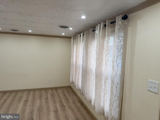 spare room featuring light wood-type flooring, visible vents, baseboards, and a textured wall