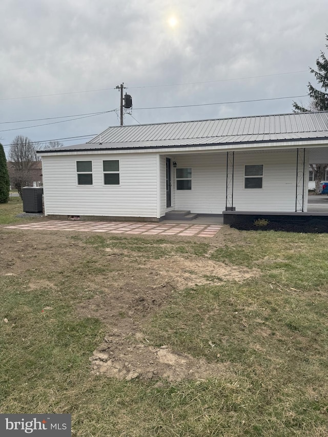 back of property with cooling unit, a yard, and metal roof