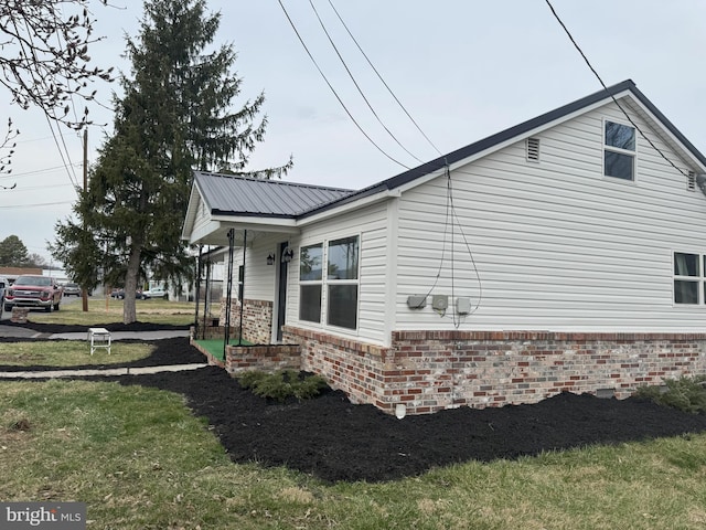 view of side of home with a lawn, brick siding, and metal roof
