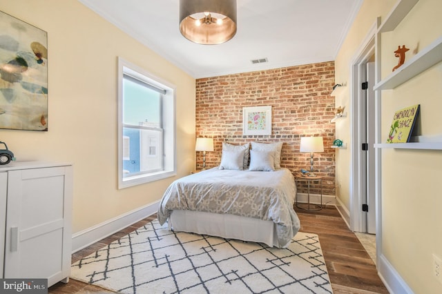 bedroom featuring ornamental molding, baseboards, brick wall, visible vents, and wood finished floors
