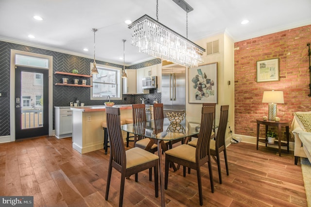 dining room featuring crown molding, wood-type flooring, brick wall, baseboards, and visible vents