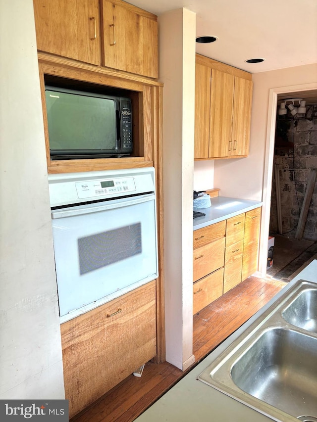 kitchen with light countertops, light brown cabinets, a sink, black microwave, and white oven