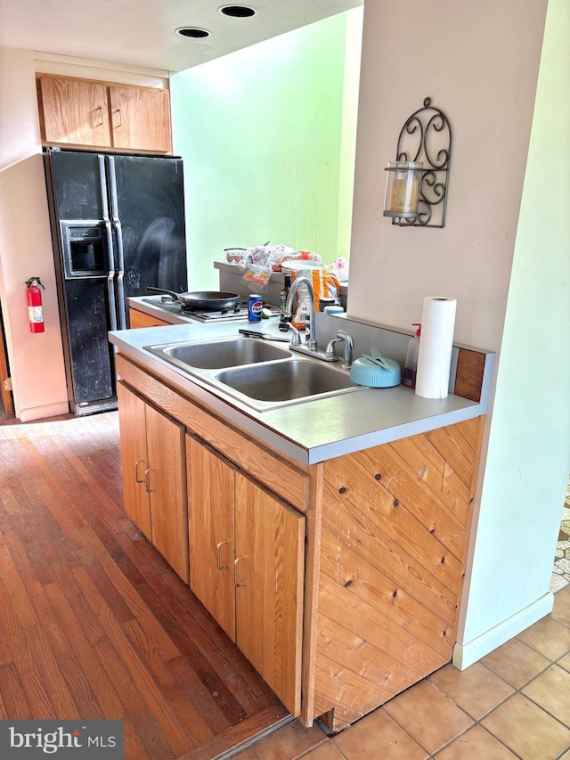 kitchen with light countertops, a sink, light wood-style floors, and black refrigerator with ice dispenser