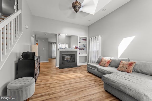living area featuring stairway, light wood-style flooring, ceiling fan, and a skylight