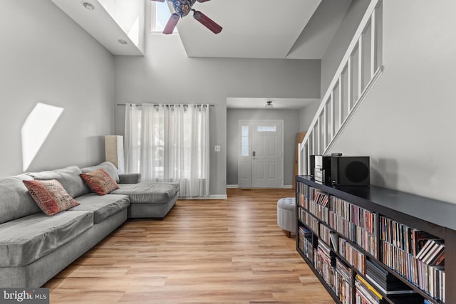living area with light wood-type flooring, baseboards, ceiling fan, and a high ceiling