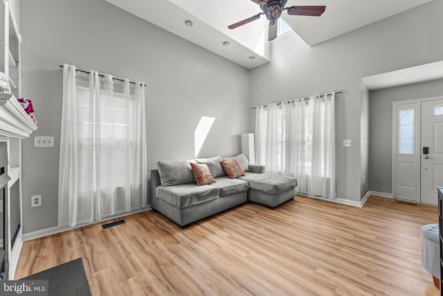 living area featuring light wood finished floors, a glass covered fireplace, ceiling fan, visible vents, and a high ceiling