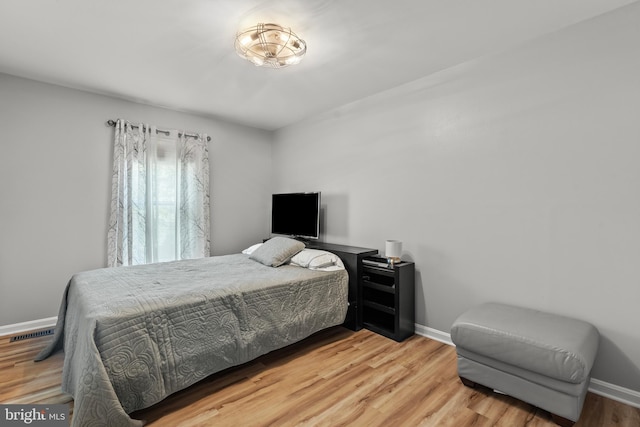 bedroom with baseboards, visible vents, and wood finished floors