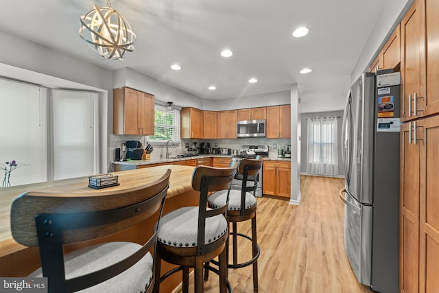 kitchen featuring a sink, stainless steel appliances, light wood-type flooring, light countertops, and decorative backsplash